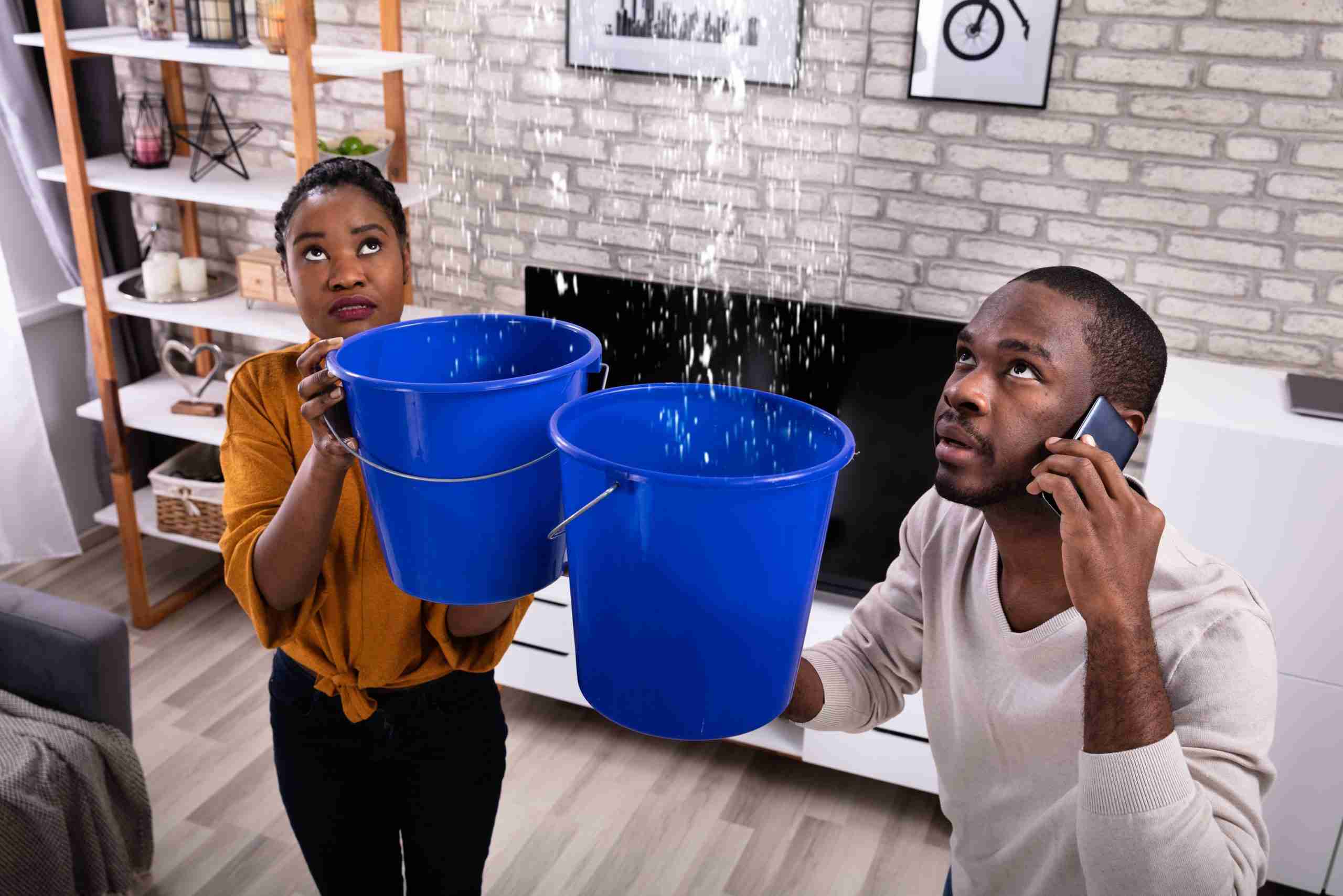 Couple catching ceiling leak water with blue buckets